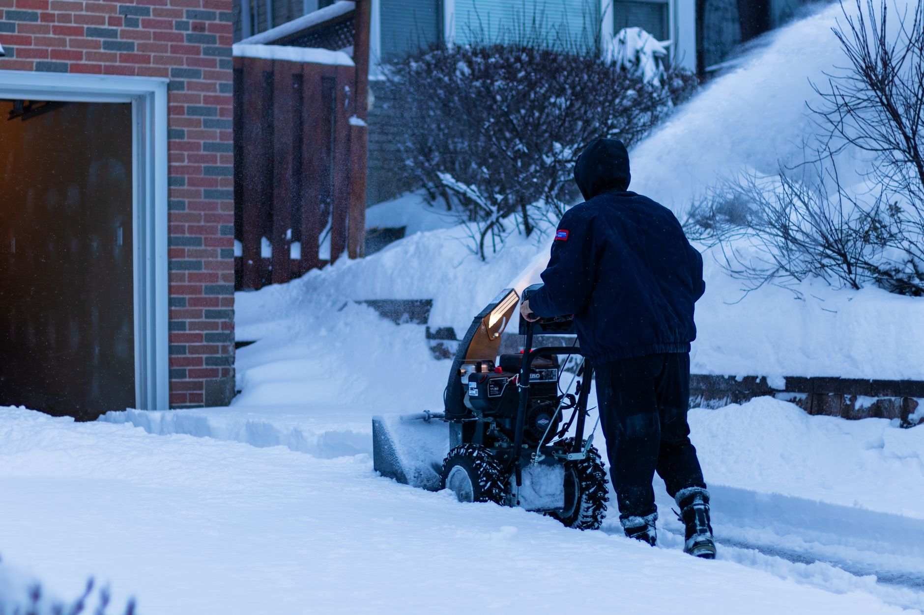 Running a snow blower along a driveway by the house
